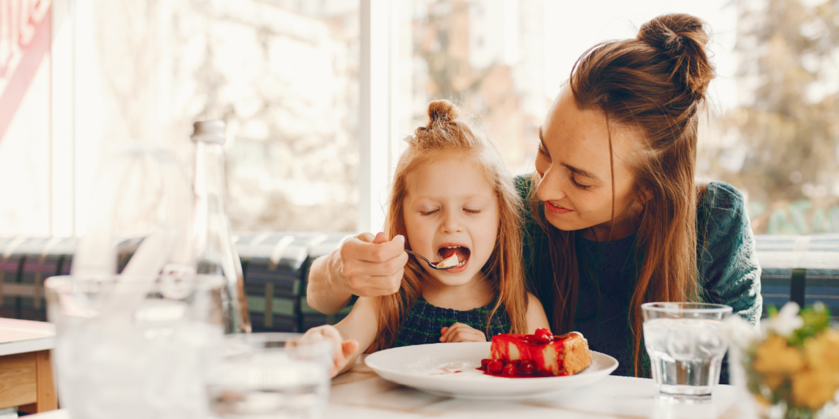 Mother feeding her daughter a piece of cheesecake